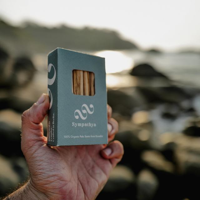 A box of Sympathya Palo Santo sticks held against the sea at sunset